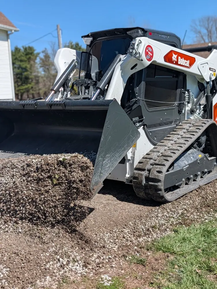 Bobcat loader using its front bucket to move soil and gravel