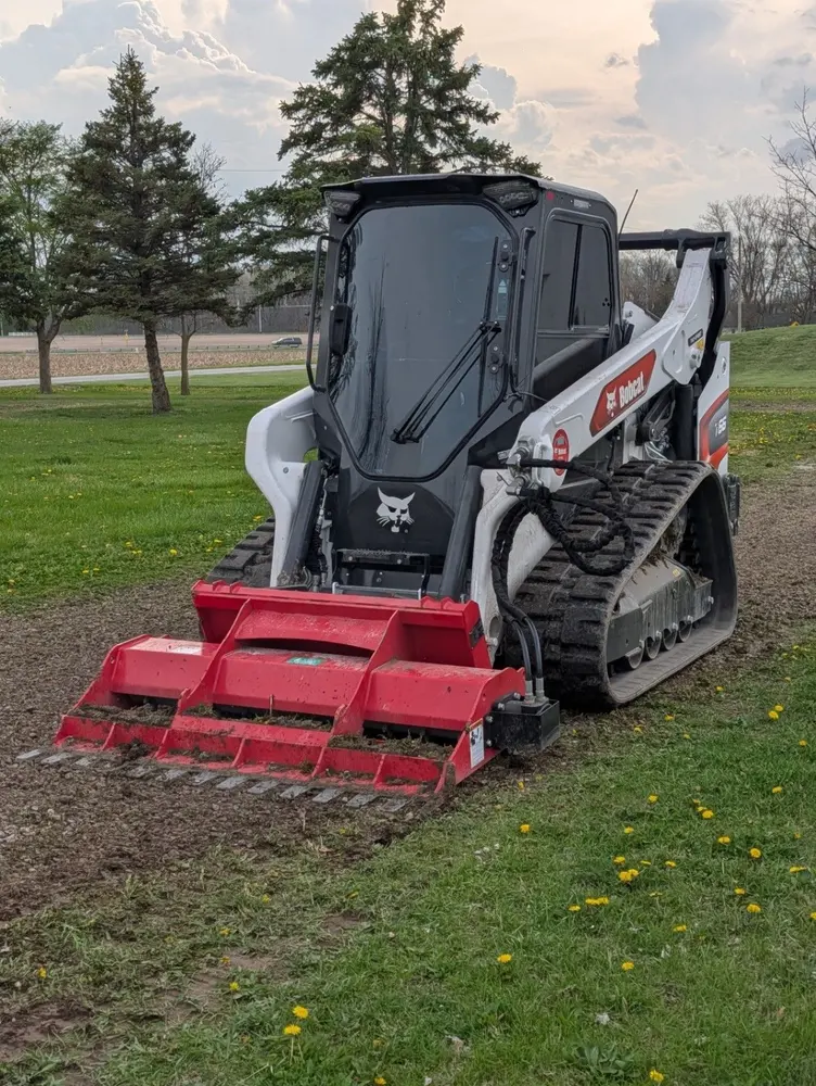 Bobcat loader working beside a truck at the edge of a tree cleanup